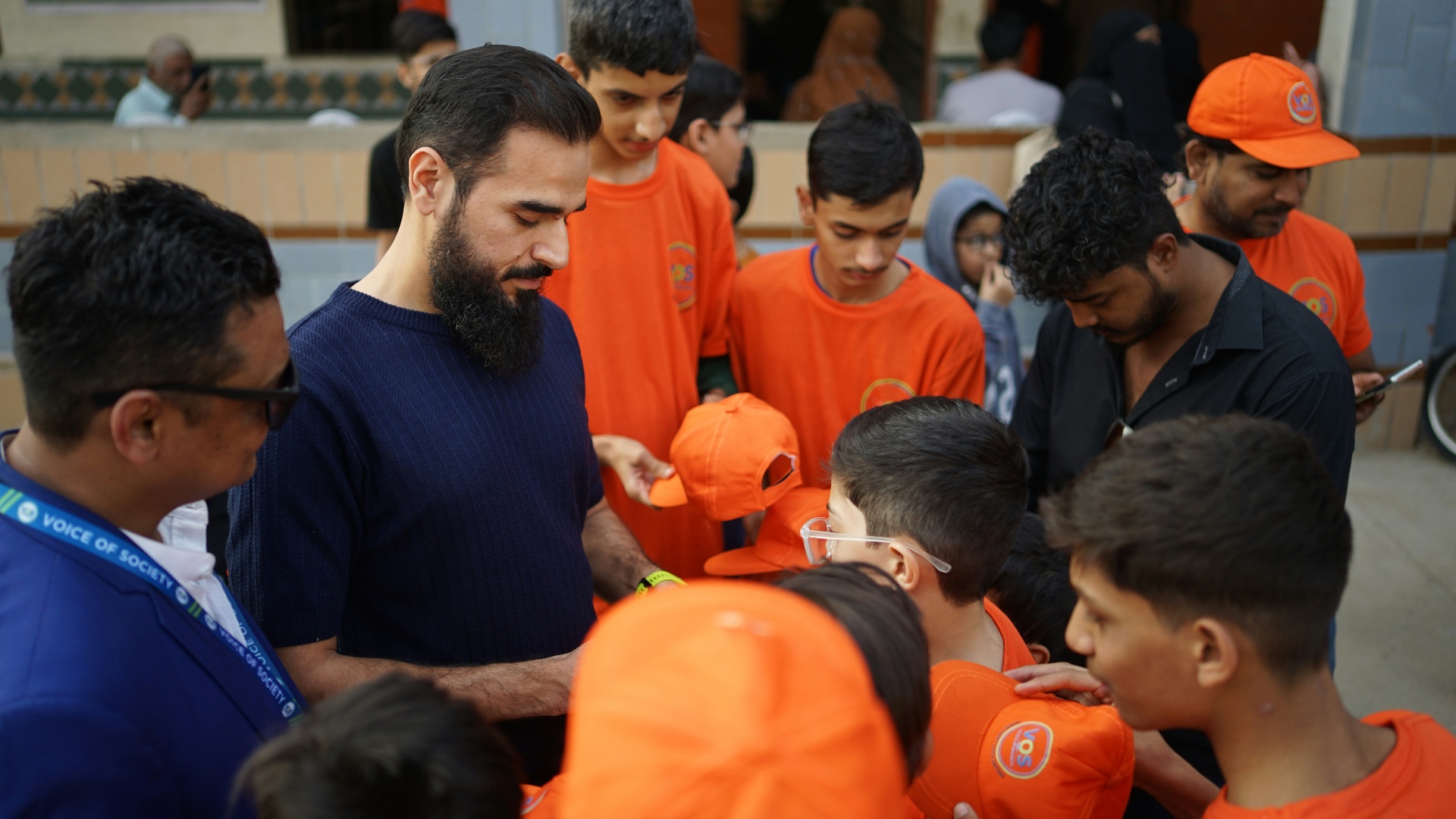 Community leader handing out branded caps to a group of young people at an outreach event